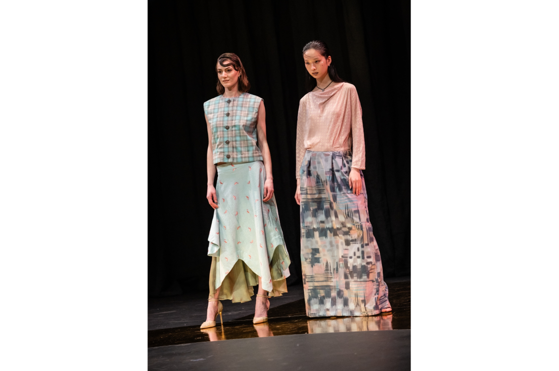 Two models pose together in pastel-colored two piece outfits with long skirts