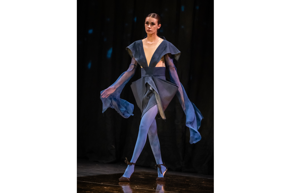 A model struts down the runway wearing a navy blue dress with cutouts at the ribs and long flowing sleeves