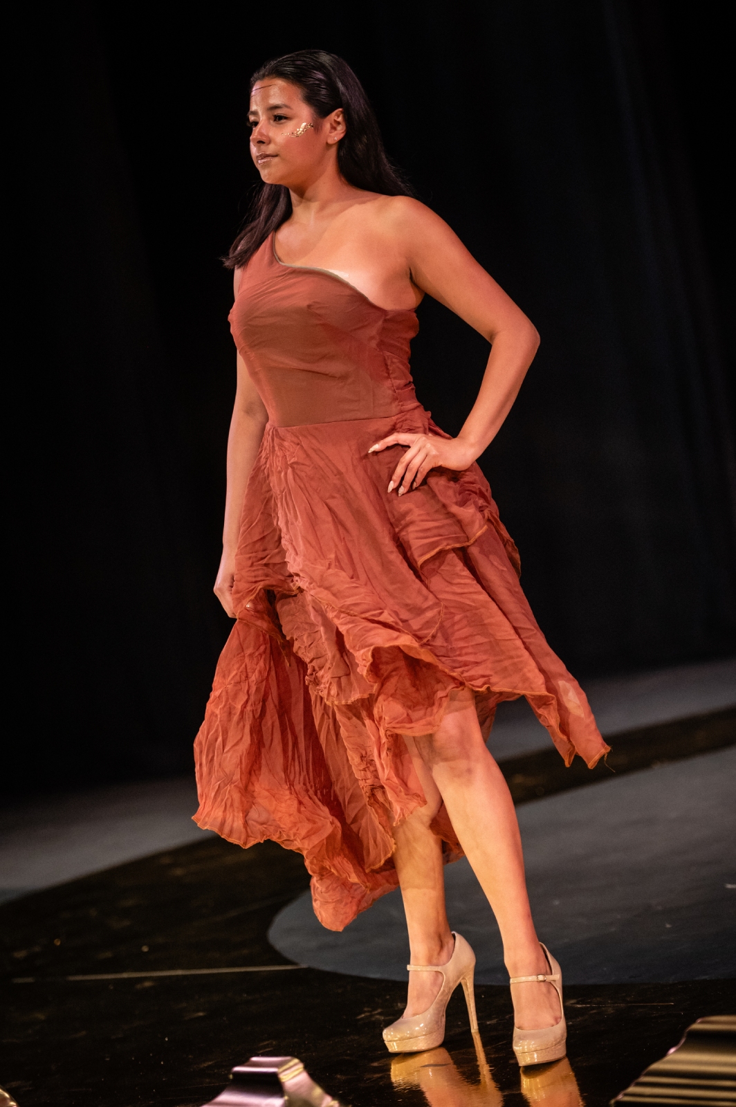 A model poses at the end of the runway in an orange dress with a layered skirt
