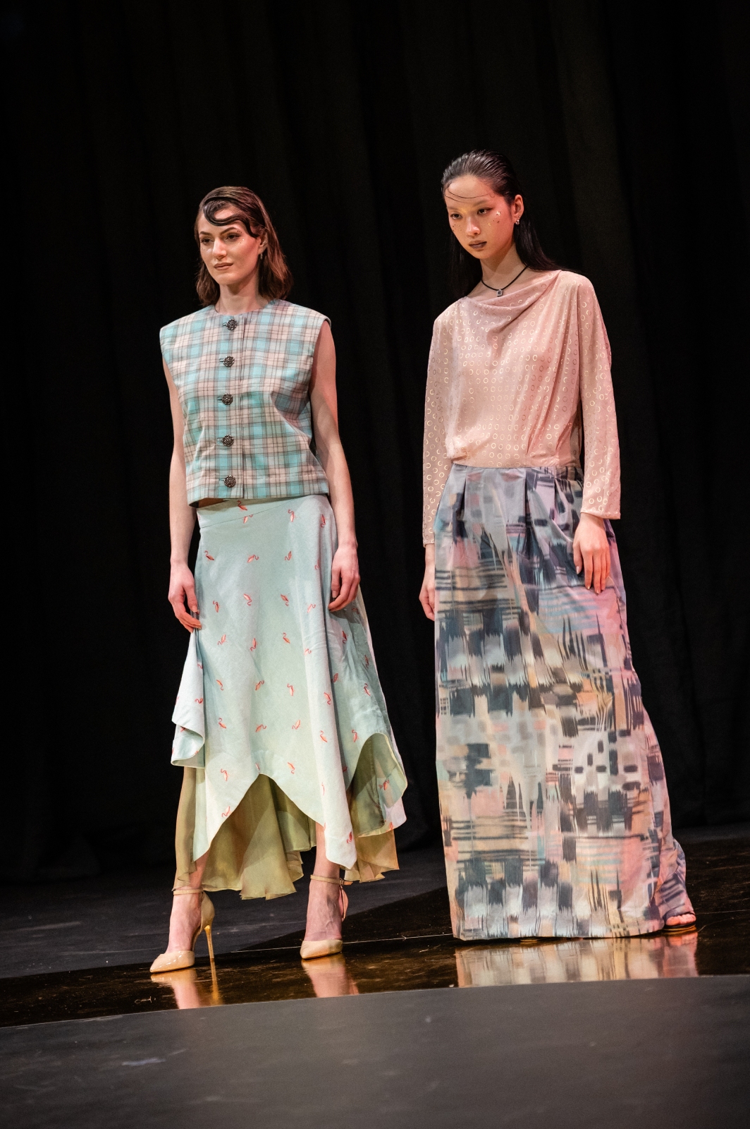 Two models pose together in pastel-colored two piece outfits with long skirts