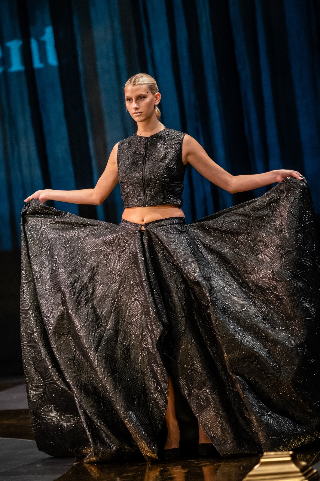 A model shows off her outfit by holding up the long skirt of her two-piece ensemble
