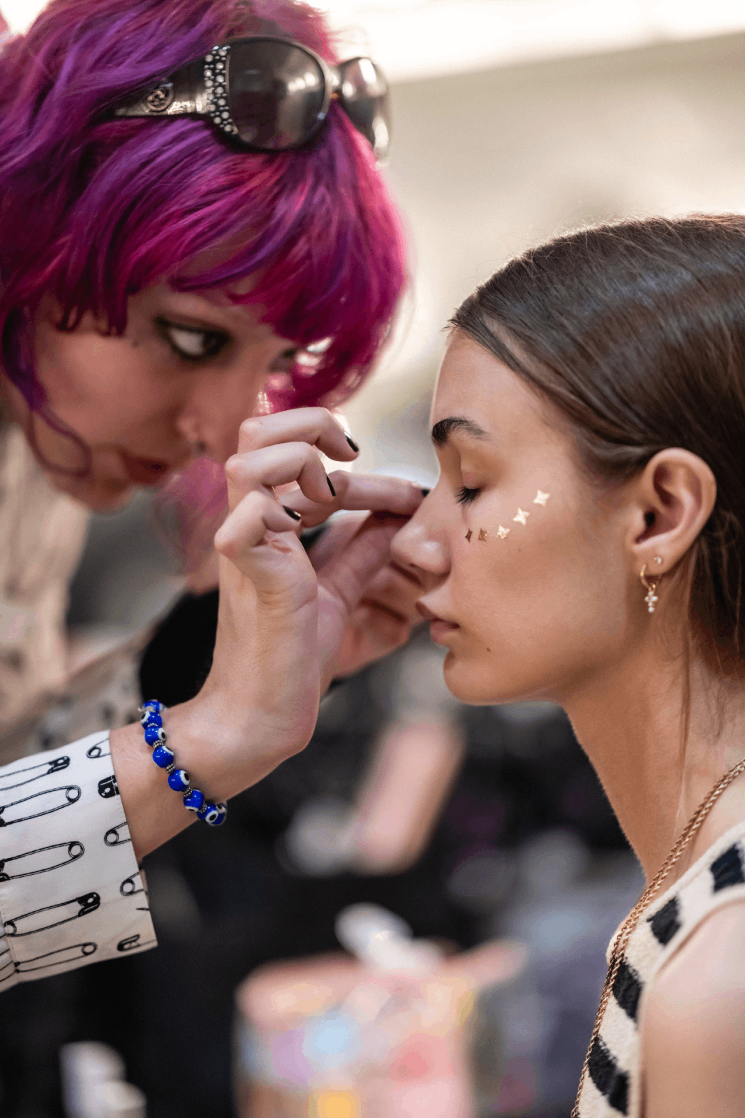 A model getting gold decal sticker put on her cheekbones by a makeup artist backstage