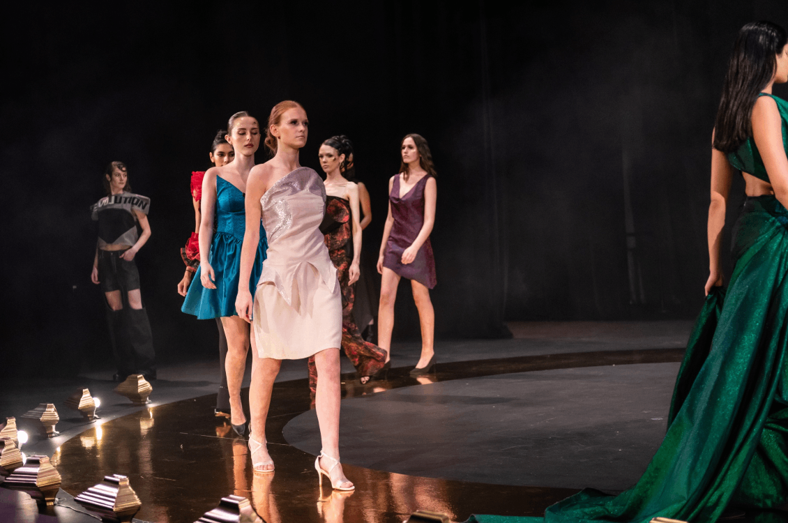 A group of models walk along the circular runway in a line
