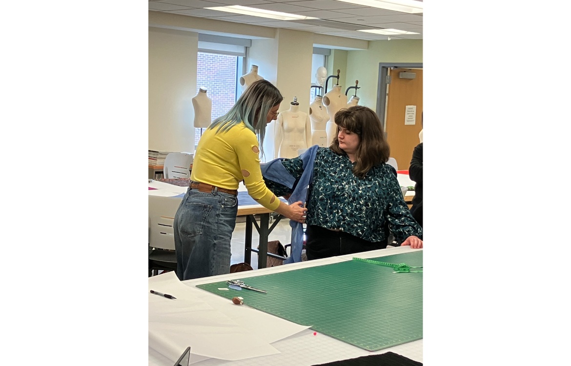 Dr. Lelaine Rigatto holding a piece of fabric up to a Fashion Studies student
