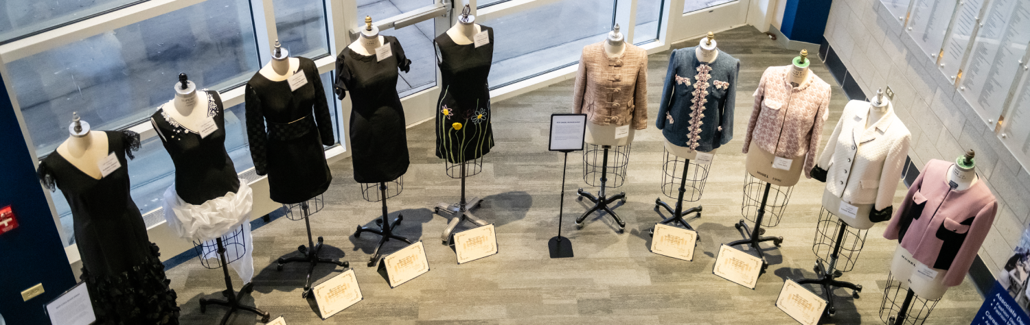 Fashion design student garments displayed on mannequins at a campus exhibit.