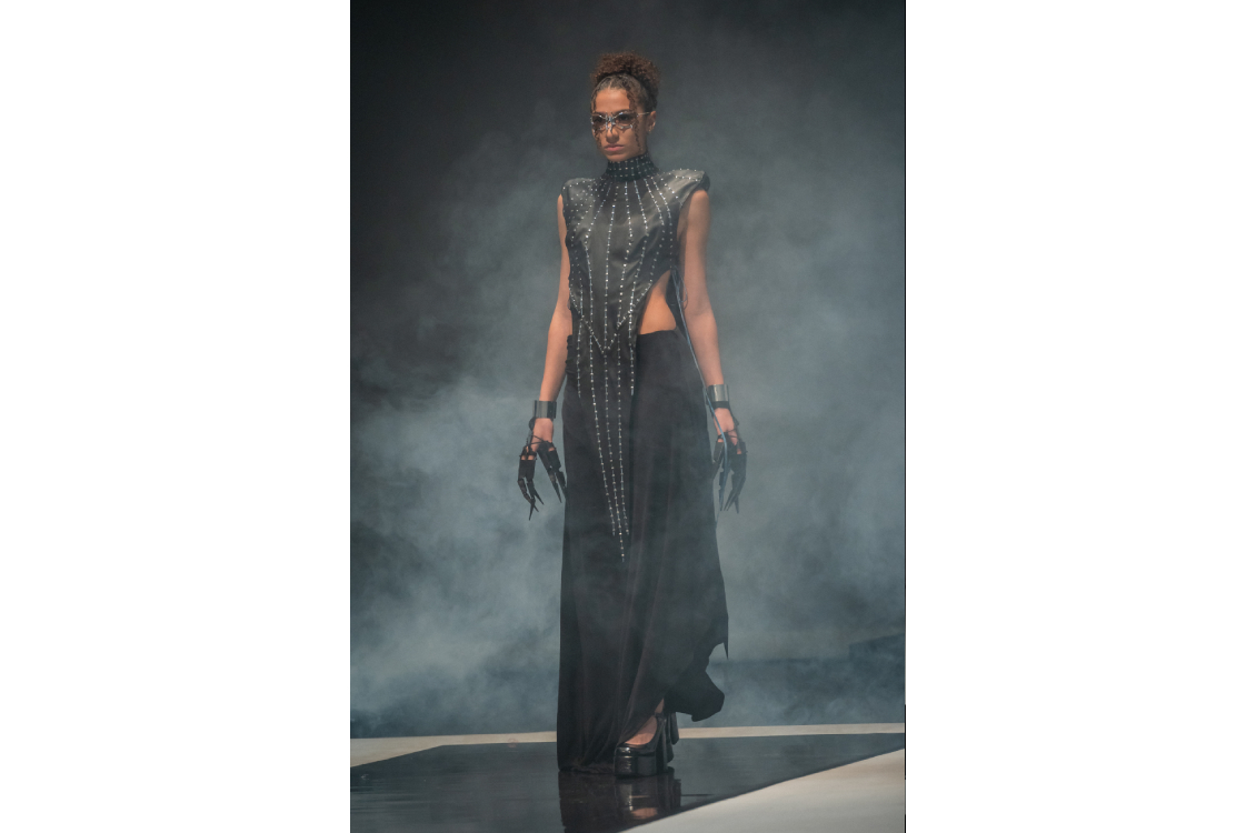 Runway model in a long black dress with studded leather bodice and claw-like gloves.