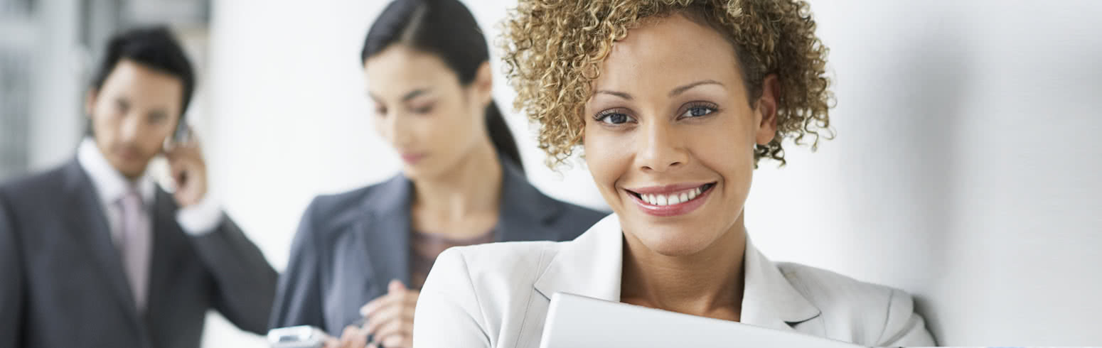 Businesswoman smiling at the camera with two business admin colleagues in the background.