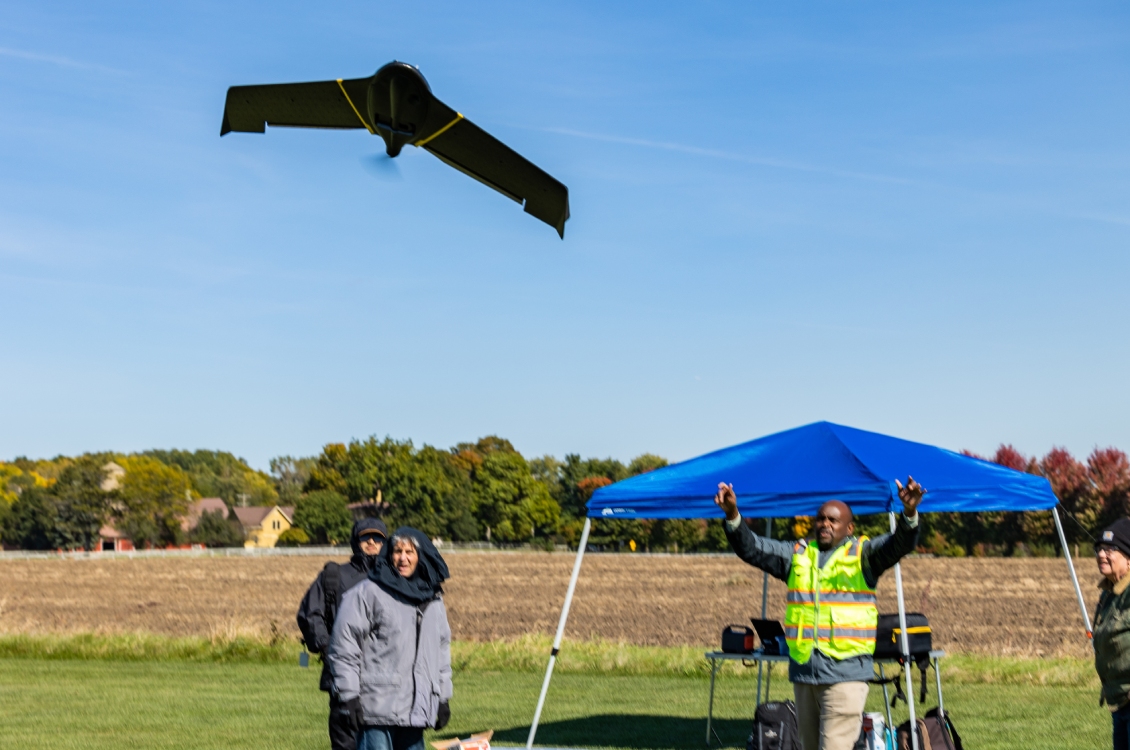 Students watch a fixed wing drone fly outside.