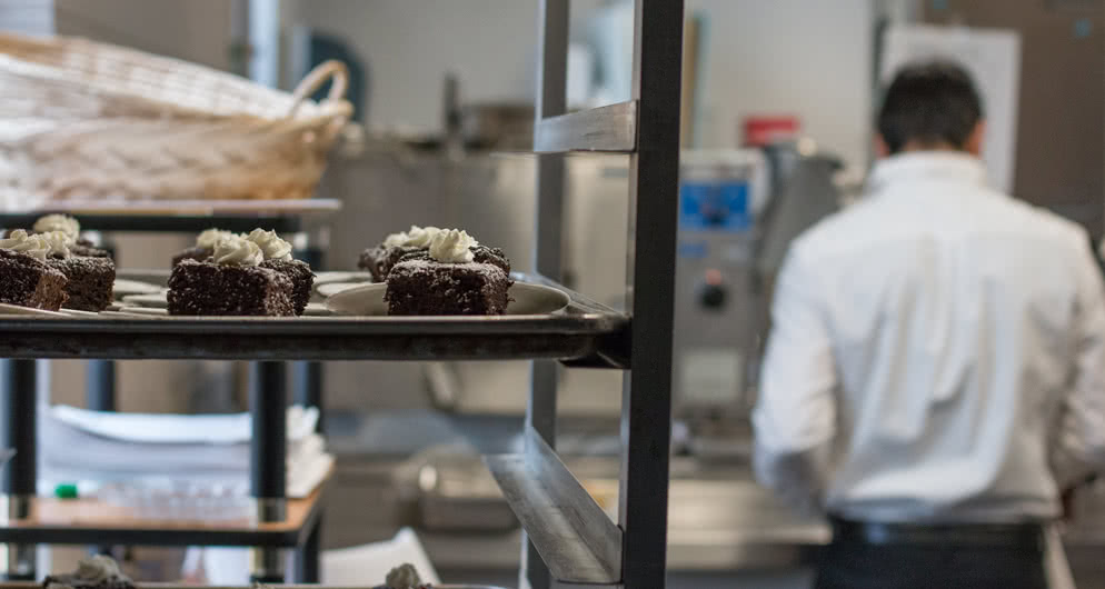 Brownies cool on a rack while a baker works in the background