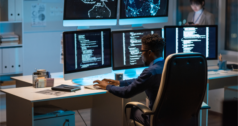 Man working at a desk with multiple monitors displaying code.