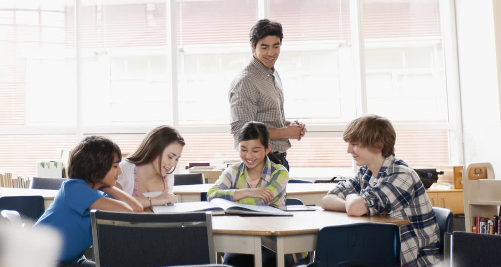 Middle school students do group work with instructor nearby.