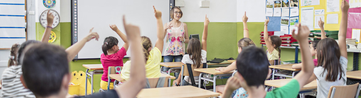 Teacher speaking to classroom full of kids with their hand raised