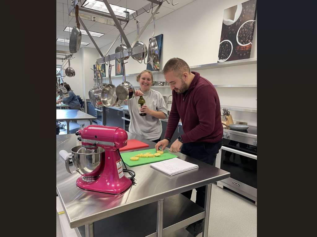 A student cuts food on a cutting board, with a large pink mixer nearby