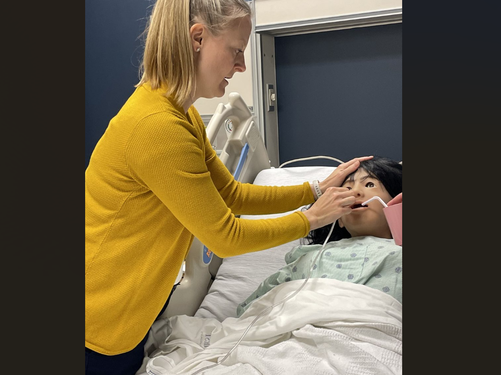 Dietetic Internship student works to "feed" a patient simulator (dummy) in a hospital bed