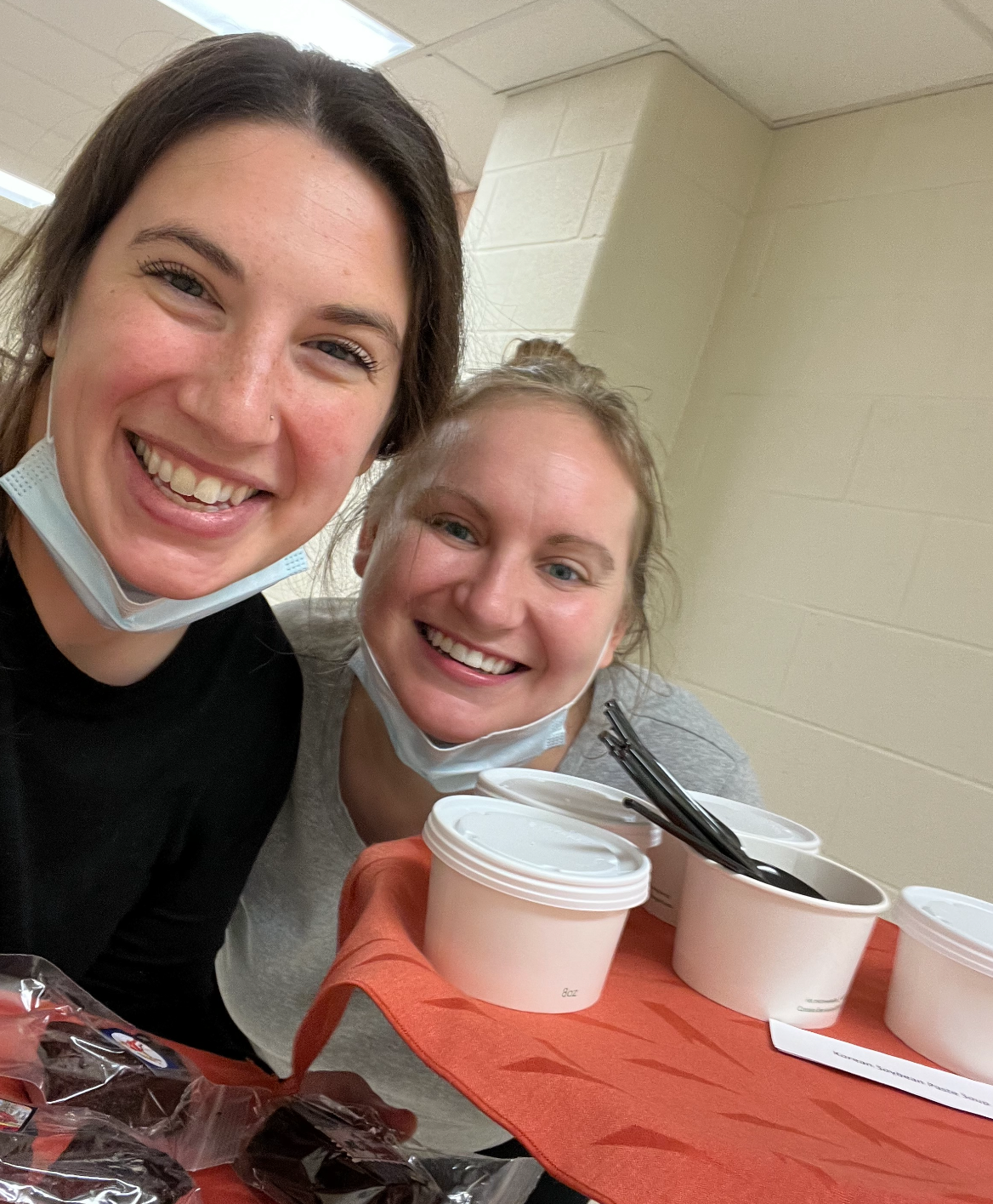 Two smiling dietetic internship students hold a serving tray with cups of food