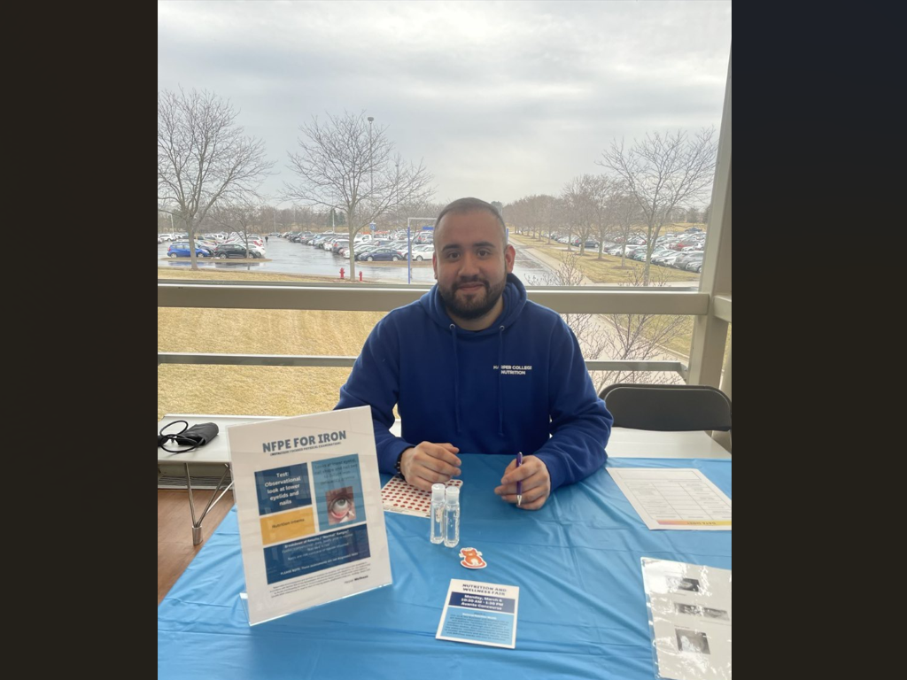 Student poses with information about Iron at a wellness event