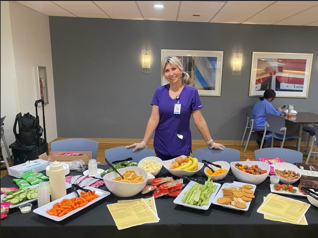 Student wearing badge poses with a spread of healthy snacks