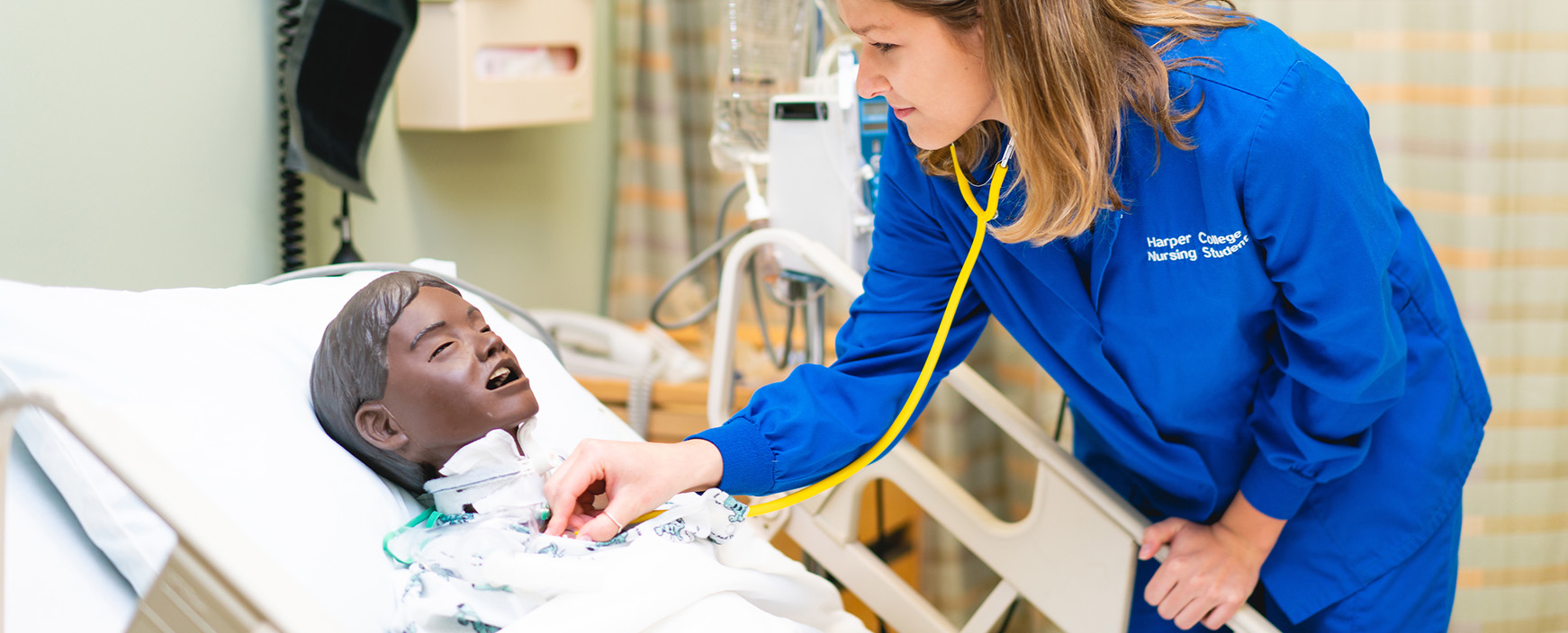 Nursing student practices using a stethoscope on a patient simulator in the healthcare classroom facilities on Harper College's campus in the Chicago suburbs.