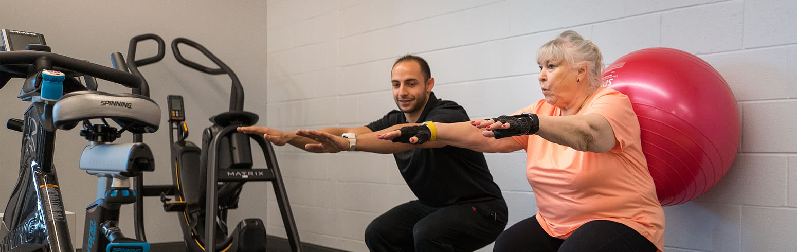 Physical Therapy school student doing squats with a patient in the gym on Harper College's campus in the Chicago suburbs.