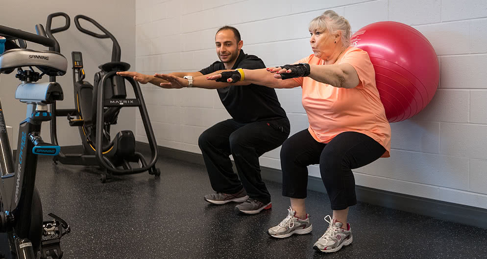 Physical Therapy school student doing squats with a patient in the gym on Harper College's campus in the Chicago suburbs.