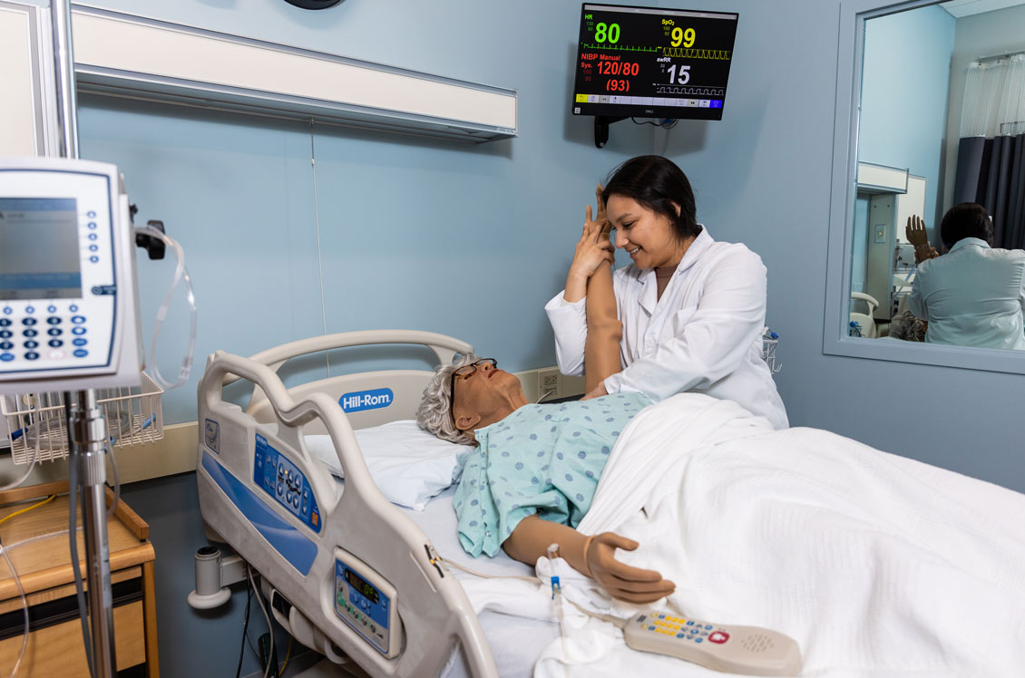 a student checks on a dummy patient in a hospital bed