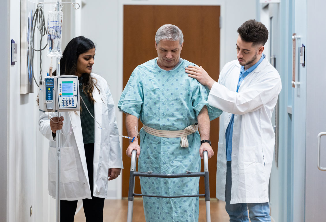Two students help a simulation patient to walk