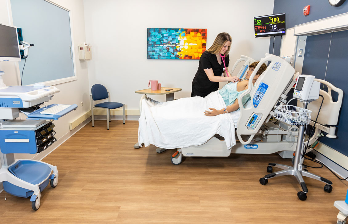 a student nurse interacts with a dummy in a simulation hospital room