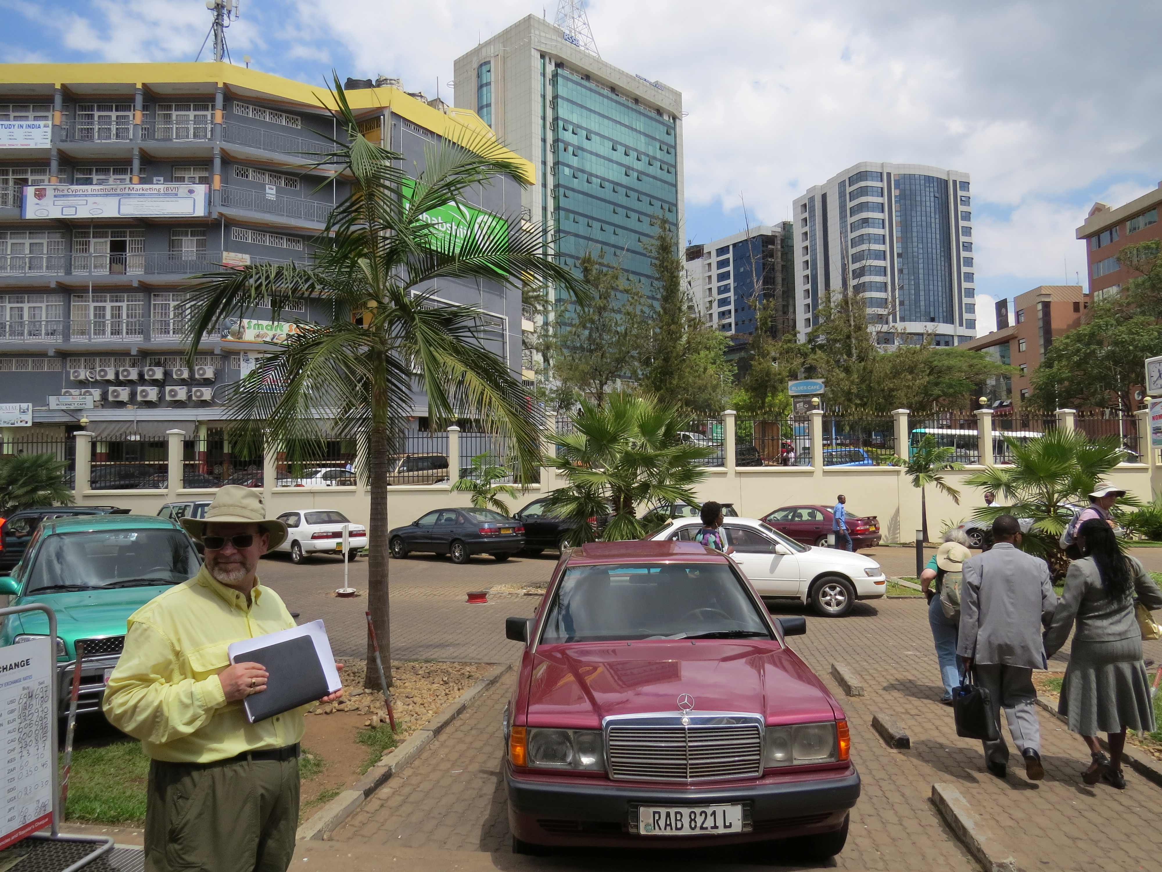 Man standing next to a car on a sunny day in downtown Kigali