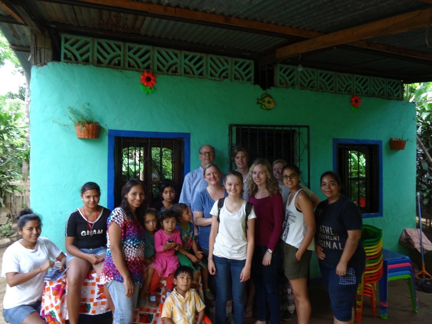 Group of students and local Nicaraguan families in front of a blue house under a patio