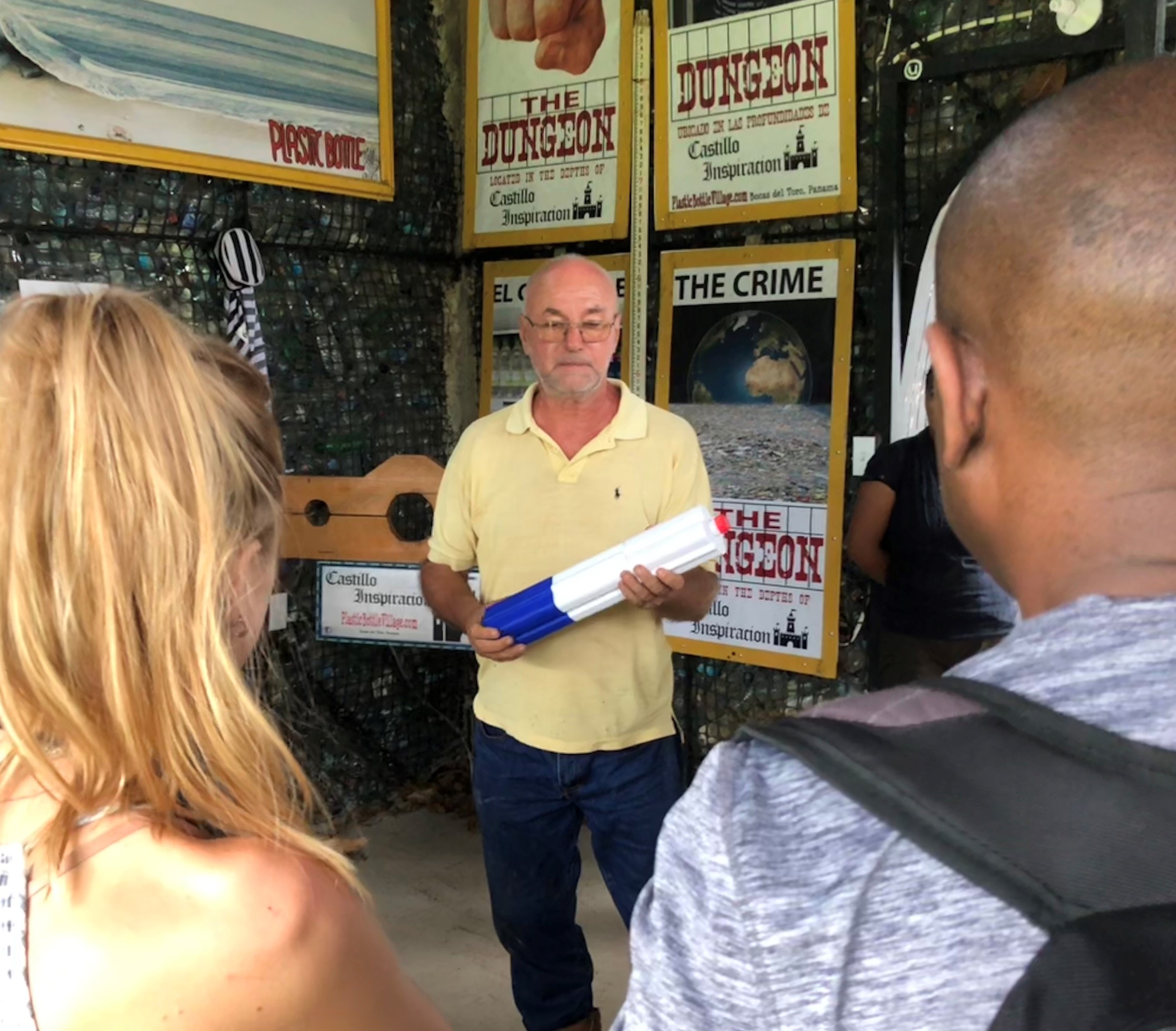 Old man holding a tube of plastic speaking to a group of students