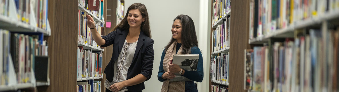 Two students walking down a library aisle