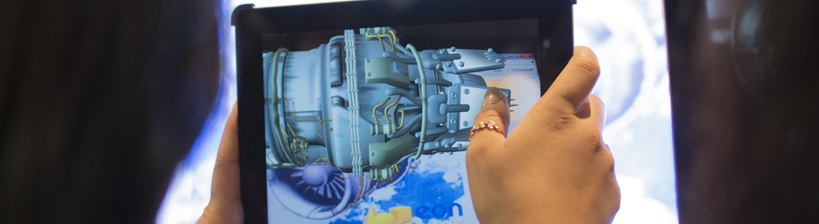 Hands holding a tablet displaying a 3D model of an engine part.