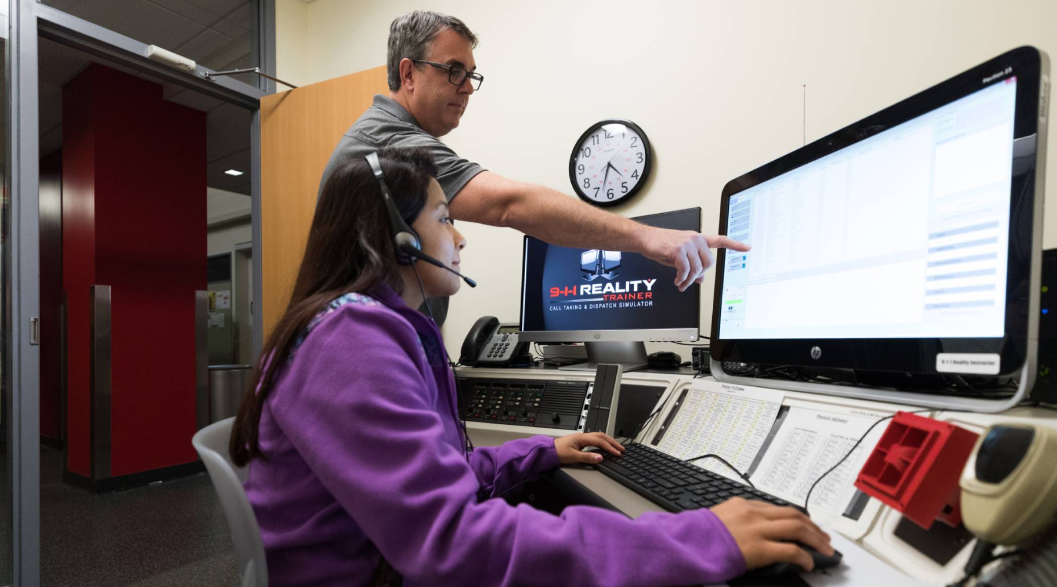 Public Safety Dispatch professor guiding a student through the 911 dispatcher training simulation program on the Harper College campus in the Chicago suburbs.