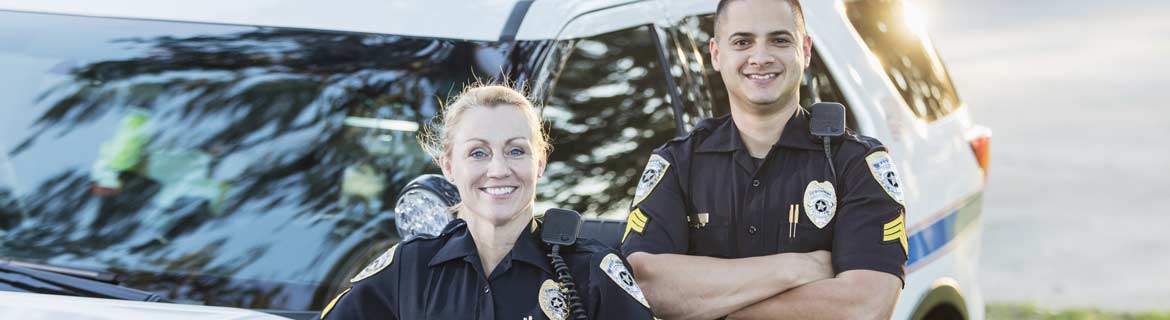 Male and female law enforcement officers stand next to a police car