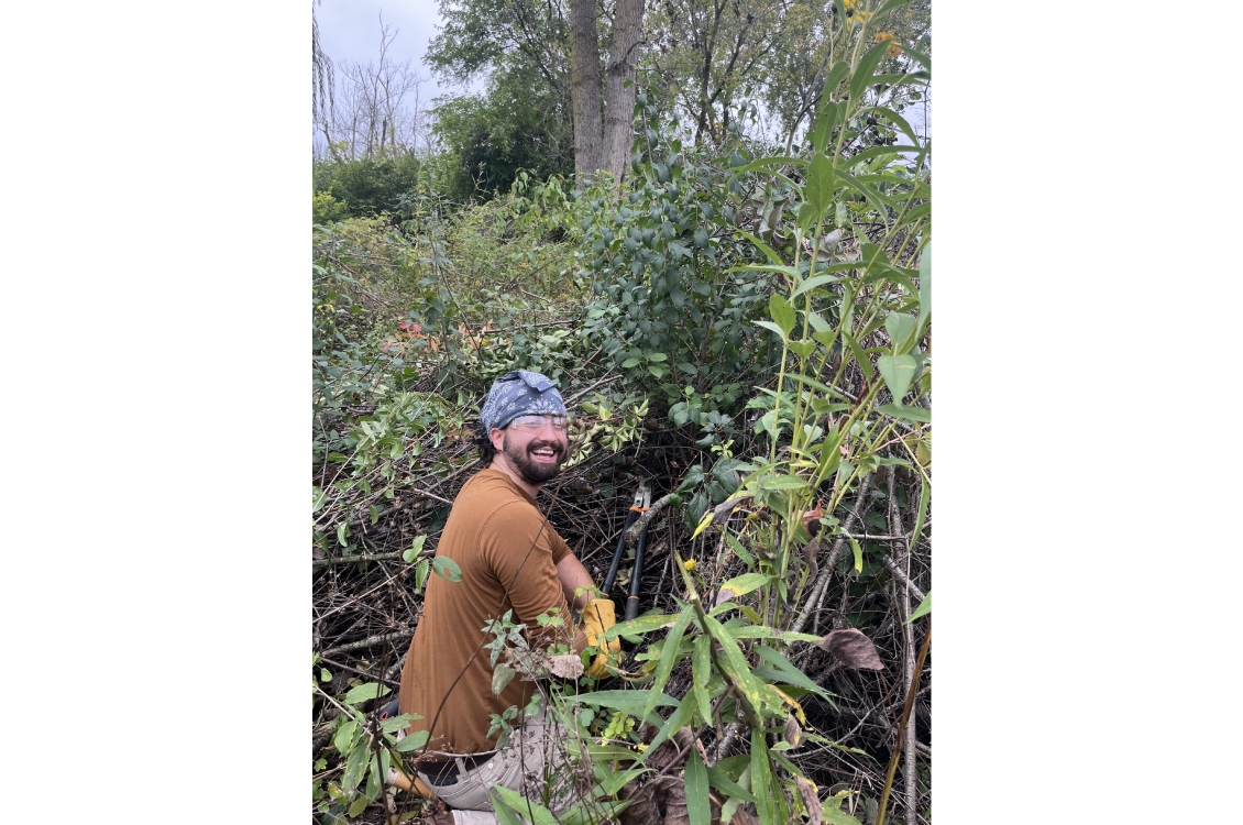 A Harper student smiles for the camera in the midst of removing invasive plant species