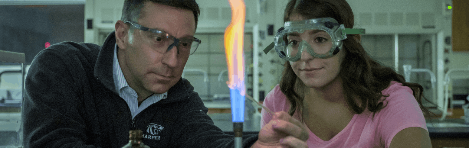 Harper Chemistry Associate Degree program student and professor heat up a chemical sample with a Bunsen burner in a science lab on Harper College's campus in the Chicago suburbs.