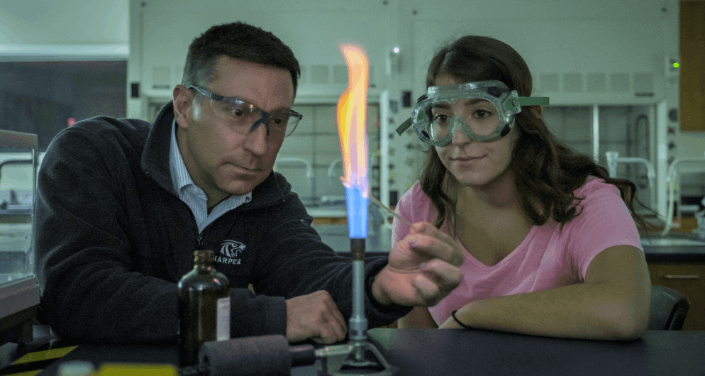 Harper Chemistry Associate Degree program student and professor heat up a chemical sample with a Bunsen burner in a science lab on Harper College's campus in the Chicago suburbs.
