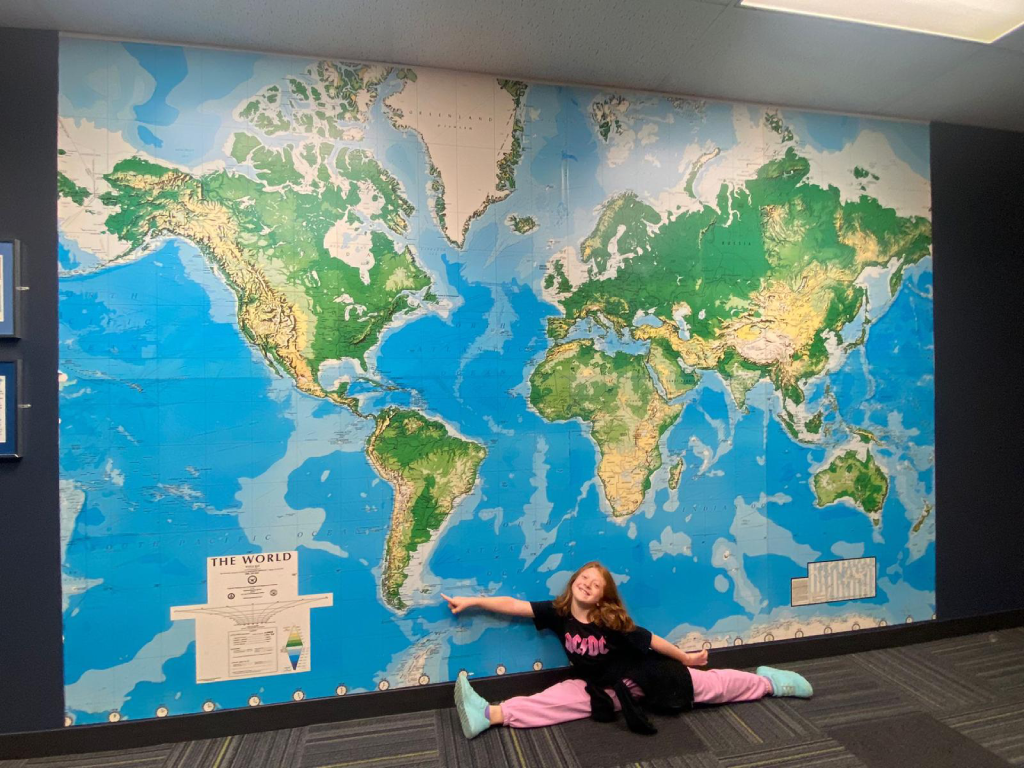 Young girl poses in front of a wall with a world map on it.