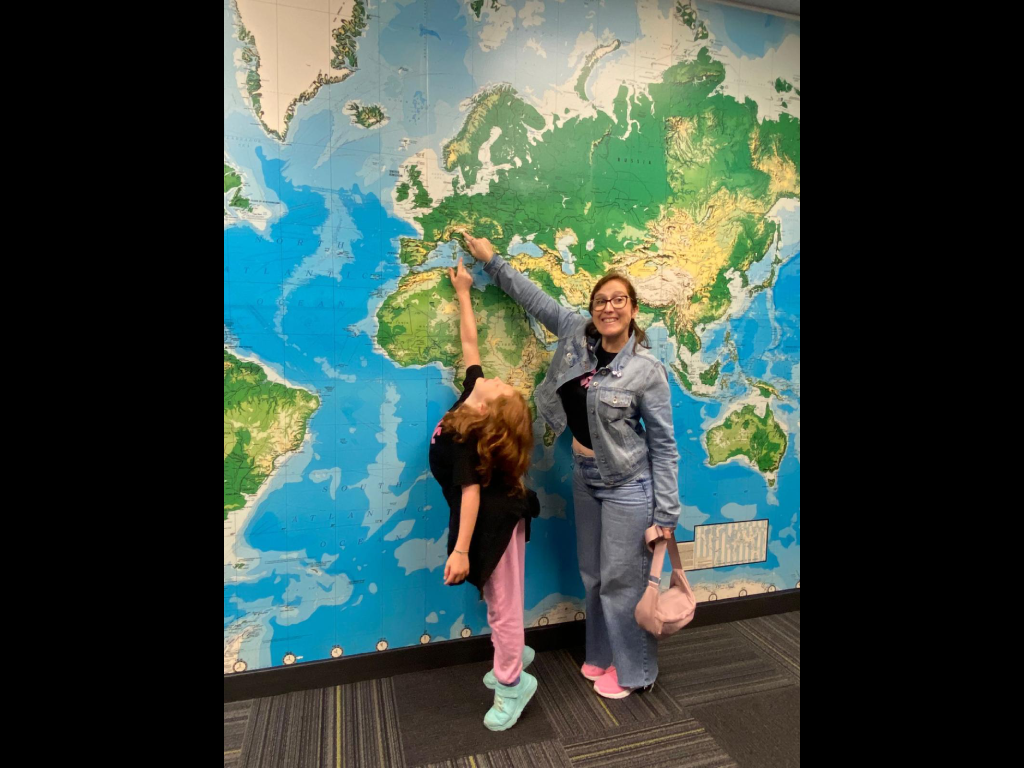 Young girl poses with a woman in front of a wall with a world map on it.