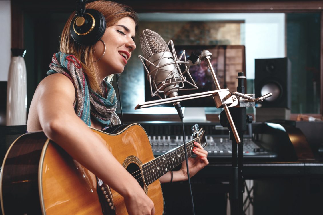 A woman playing guitar and singing into a microphone in a recording studio