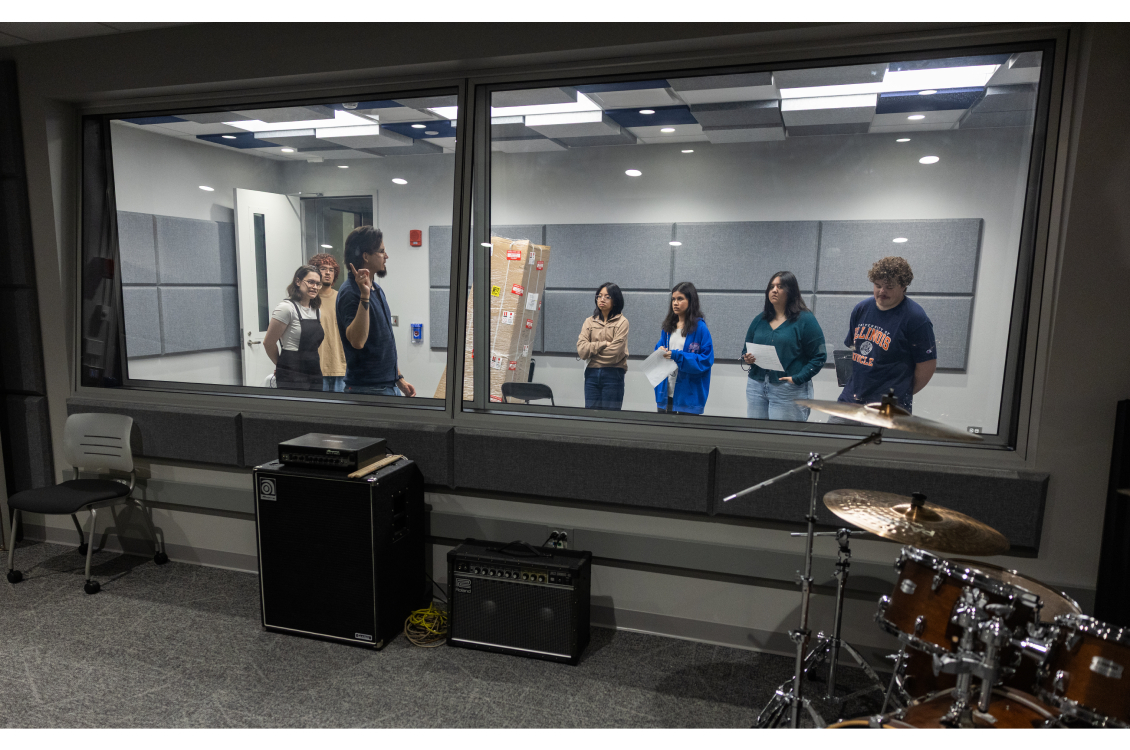 Music students stand in the recording booth and listen to an explanation about the technology