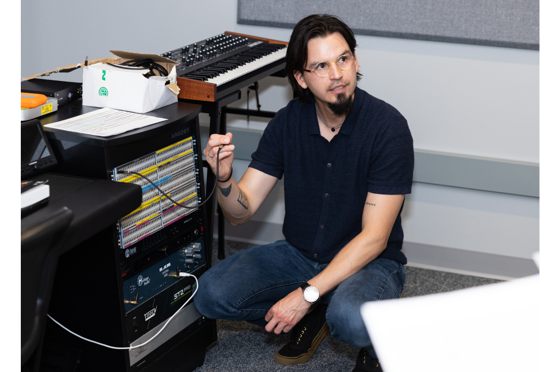 Instructor Edward Hamel holds a cord and explains that piece of tech to music students