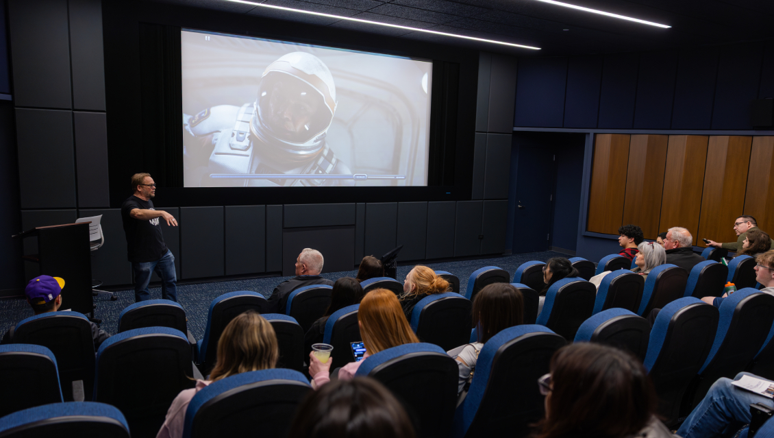 A film class in session and taking place in the Movie Screening Room/Film Lab at Harper College, where students listen as a professor lectures about a film