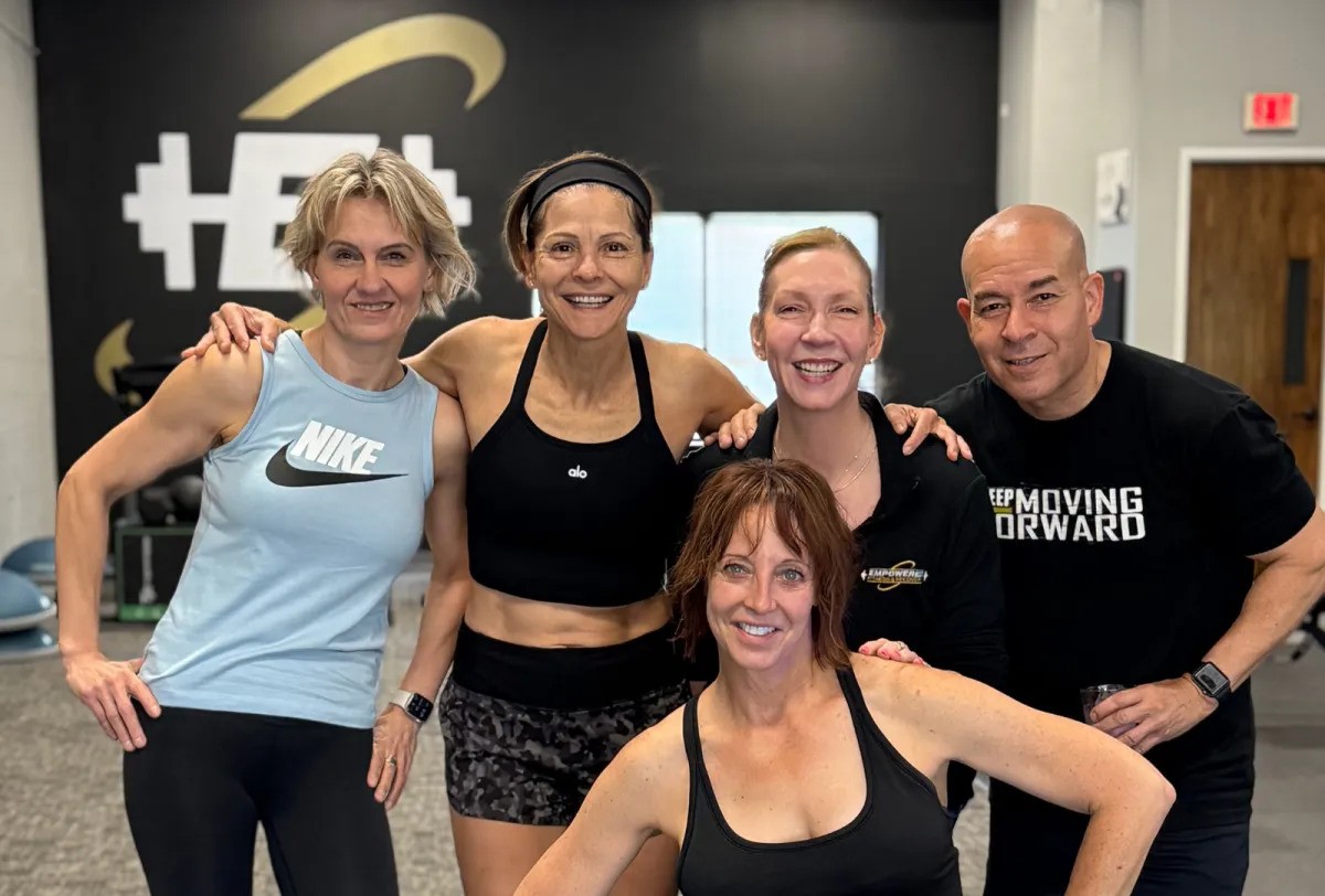 A fitness group from Empowered Fitness & Recovery, LLC stand in a group formation in their exercise facility and smile for the camera