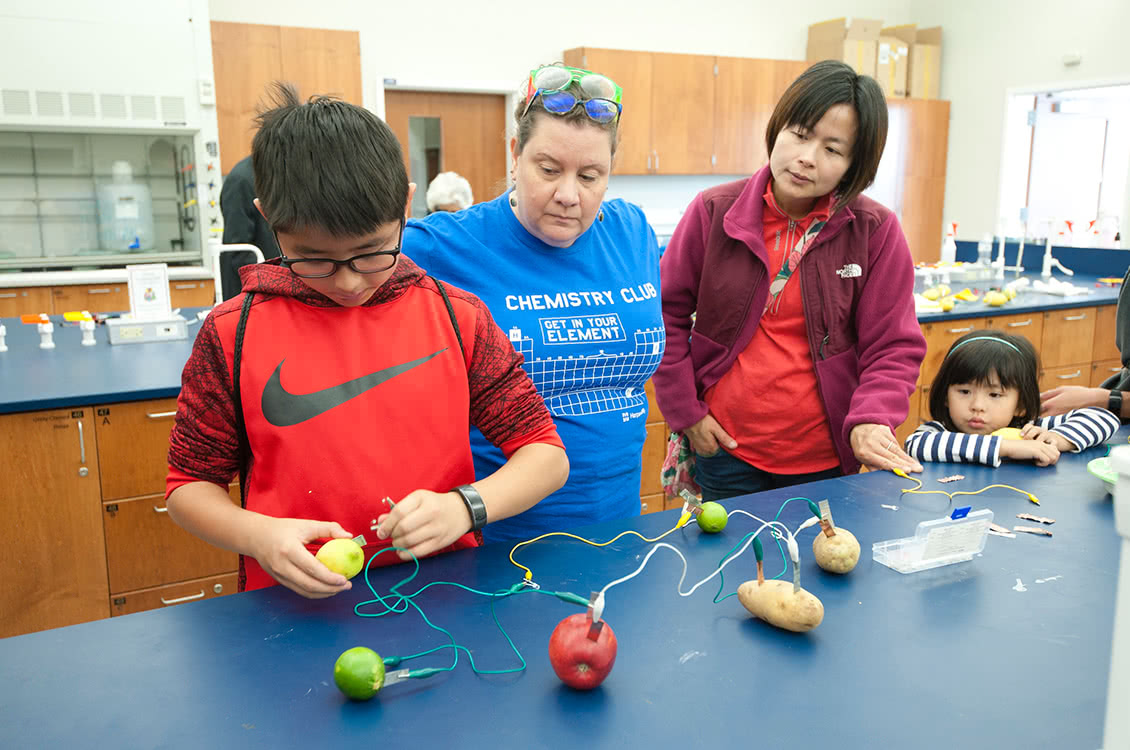 An instructor assisting children and their parent with an experiment.