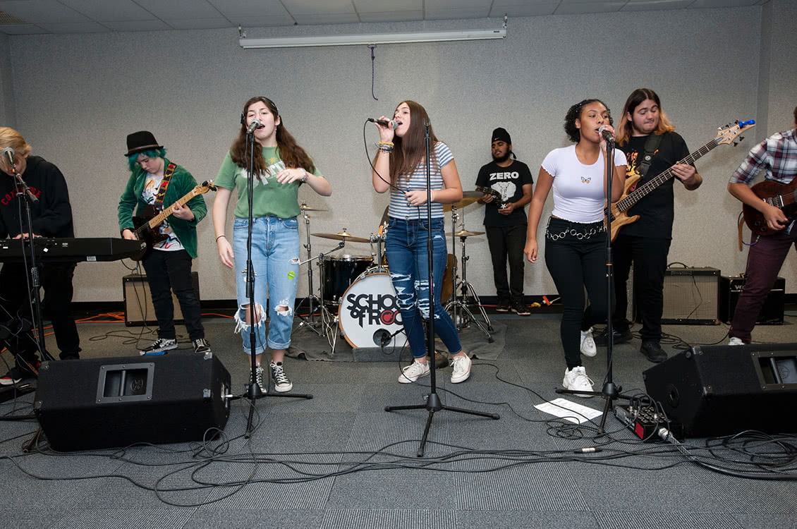 A group of three women singing with a live band playing behind them.