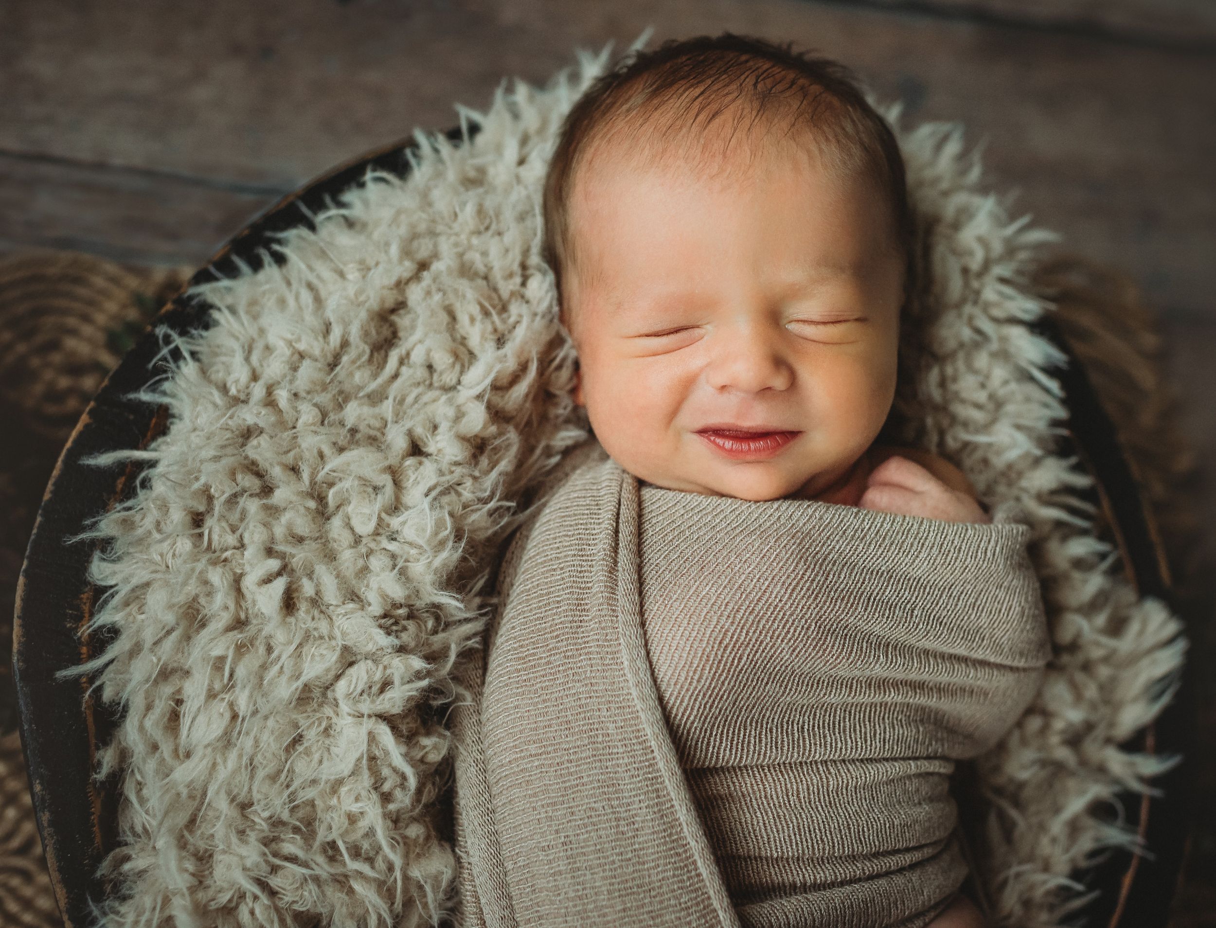 Baby Noah swaddled in a brown basket asleep with his hand sticking out.