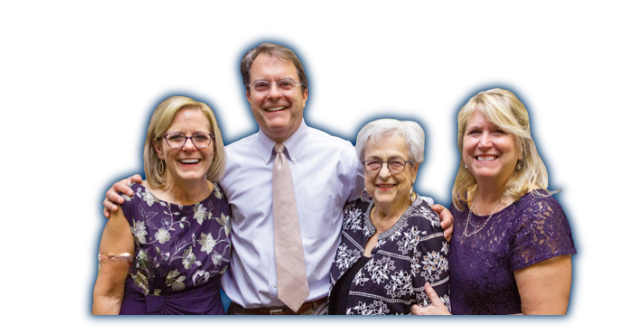 Four smiling people with arms around each other's shoulders wearing business casual clothes.