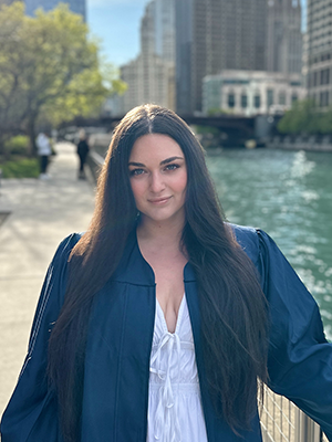 Ortal poses in graduation robes along the Chicago River