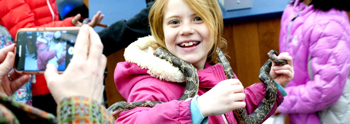 Girl poses with snake while mom takes picture at College and Career Expo
